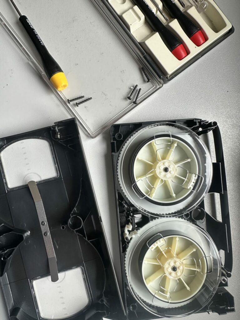 Cassette VHS démontée montrant le mécanisme de la bande et des tournevis de précision