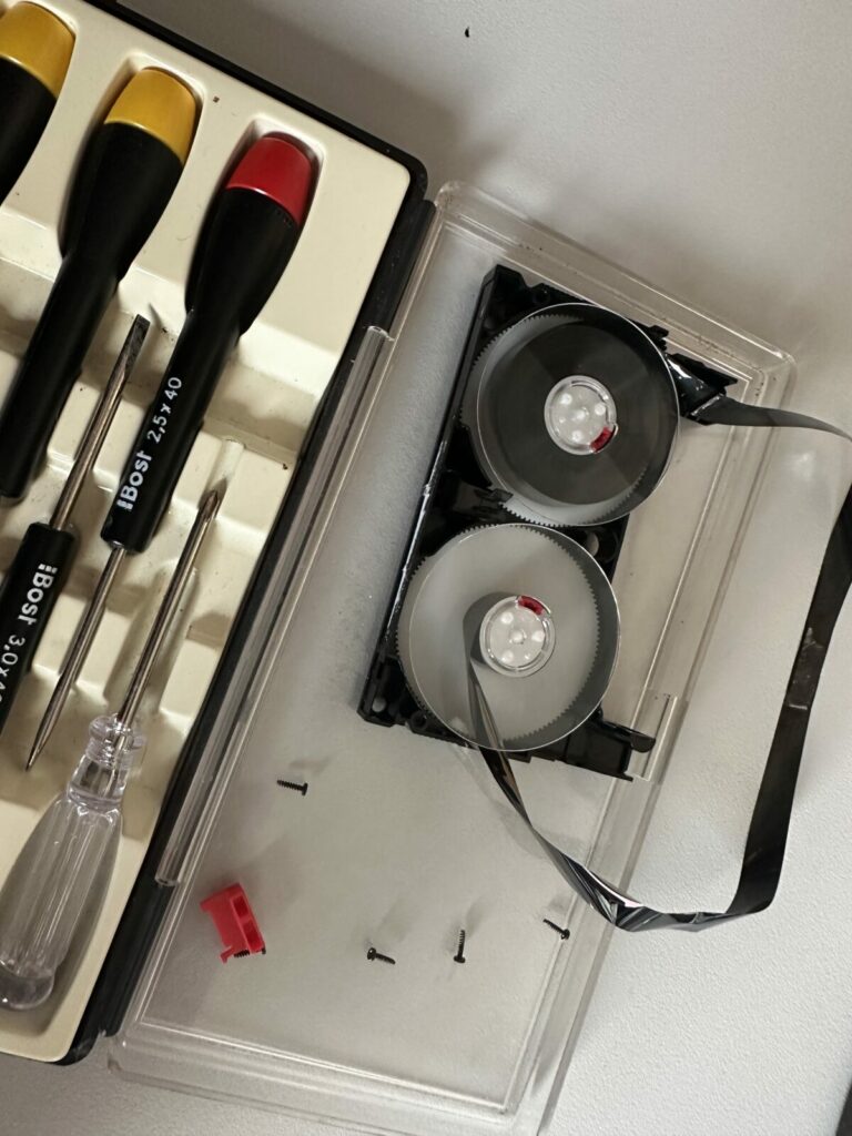 Cassette vidéo démontée avec bande magnétique emmêlée et tournevis de précision au studio 3V Movie